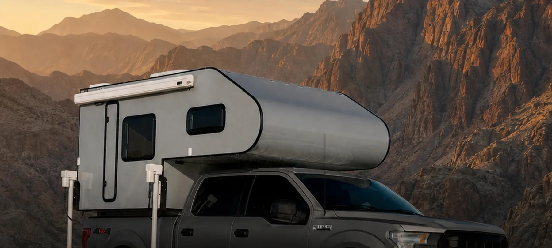 Leman ATLAS slide-in camper mounted on a pickup truck against a UAE mountain backdrop at sunset